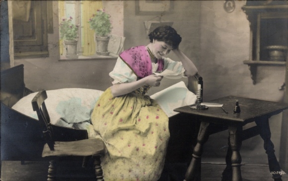 Postcard woman at the table reading a letter, living room, folk costume