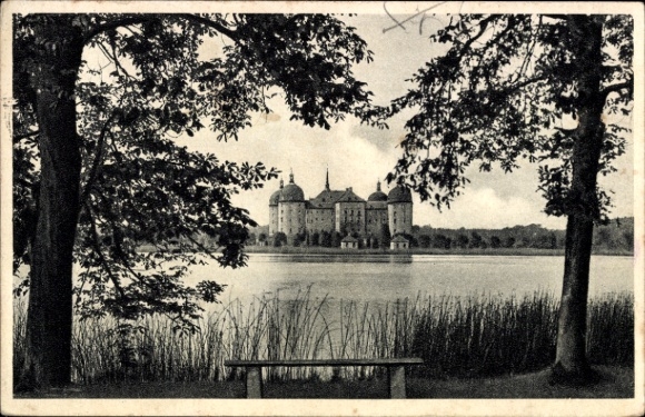 Postcard Moritzburg in Saxony, hunting lodge water view, trees in the foreground, bench on the shore