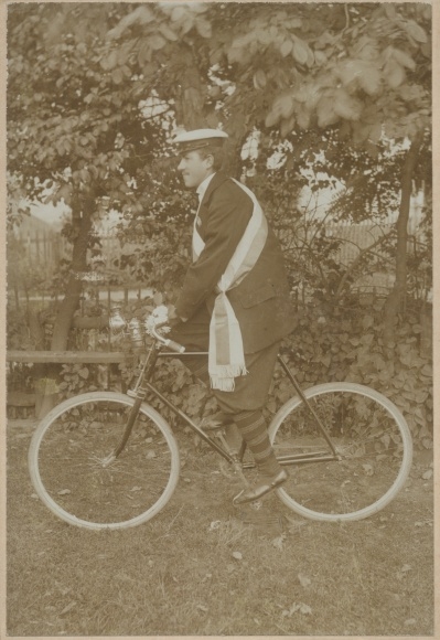 Photo student on a bicycle, flat cap, sash