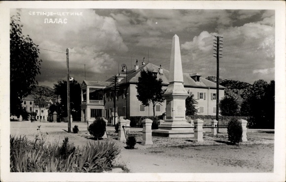 KP Cetinje Montenegro, obelisk, budynek w tle, otoczenie przypominające park, zachmurzone niebo