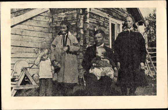 Postcard Family in traditional costumes in front of a wooden house, grinding stone