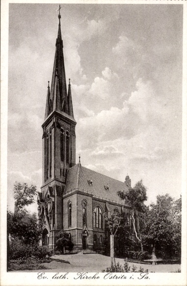 Ak Altstadt Ostritz in Sachsen, Ev. luth. Kirche, gotischer Stil, hohe Spitze, Bäume im Vorder...