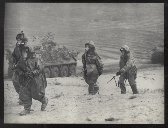 Photography DDR NVA soldiers in protective gear during a maneuver, tanks in the background