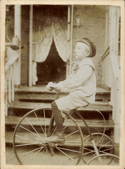 Photo boy on a tricycle, high wheel, entrance steps of a house