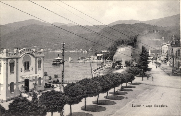 Ak Luino Lago Maggiore Lombardia, Lago Maggiore, Hafenansicht, elegantes Gebäude, Berge im Hinter