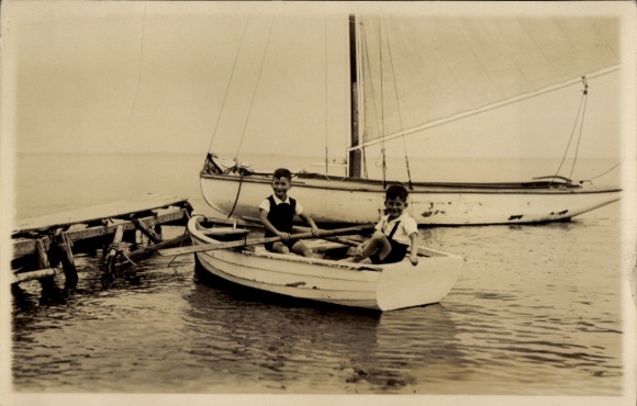 Ak Ostseebad Timmendorfer Strand, Junge auf einem Boot, Segelboot im Hintergrund, ruhige Wasserob