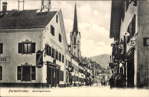 Postcard Partenkirchen in Upper Bavaria, street with shops, church in the background, atmosphere