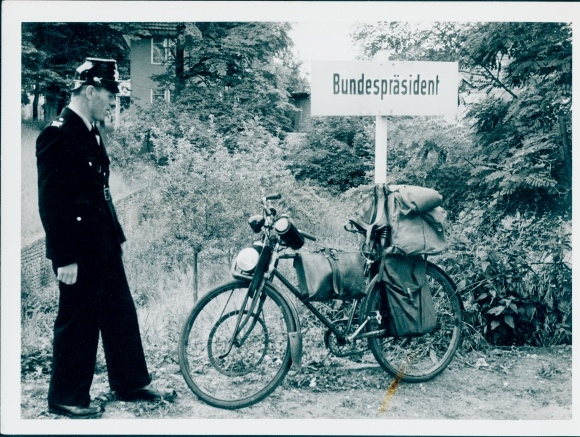 Photo Police officer in uniform, loaded bicycle leaning against a sign with the inscription Federal President
