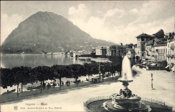 KP Lugano Kanton Ticino Szwajcaria, nabrzeże, góra w tle, fontanna, promenada nadbrzeżna