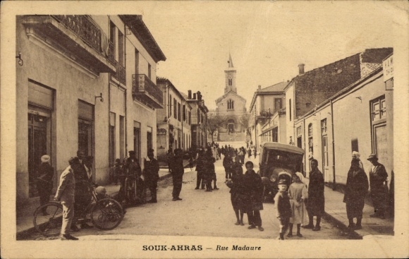 Ak Souk Souq Ahras Algerien, Straße mit Menschen, Kirche im Hintergrund, alte Autos,  Szenerie