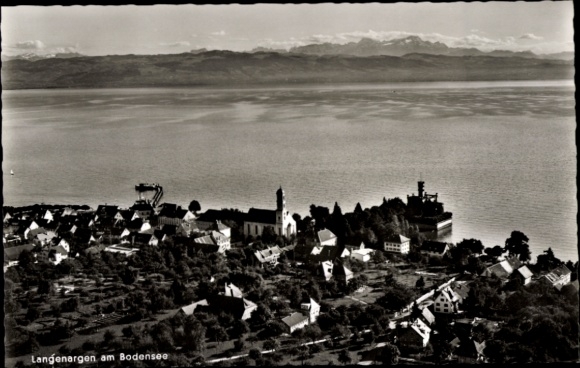 Ak Langenargen am Bodensee, Luftaufnahme, Bodensee, viele Bäume, Häuser, Kirchturm, Berge im Hint