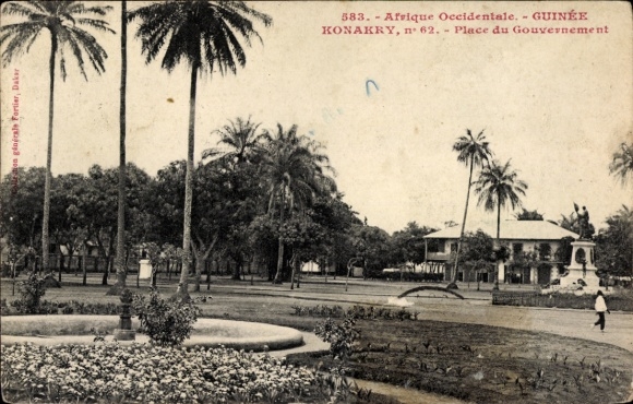 Ak Conakry Konakry Guinea, Place du Gouvernement, palmbomen, standbeeld, bloembed,