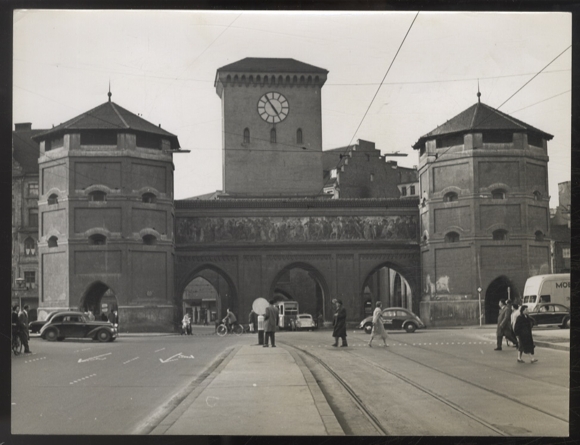 Photograph of a street scene with cars, trams, pedestrians in front of Munich's Isartor, around 1950